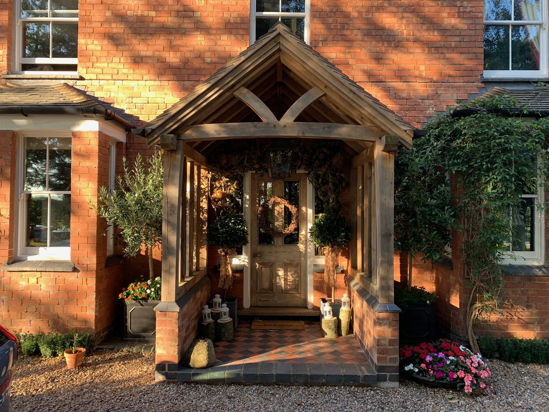 Timber porch with a wreath, seasonal greenery, lanterns and flowers framing the entrance.